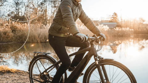 Mandlig cyklist på vej på arbejde, cykler langs sø oplyst af morgensolen